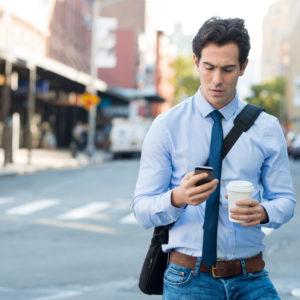 man on his phone and holding a coffee in urban area