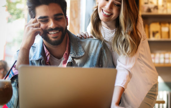 happy couple looking at laptop in coffee shop