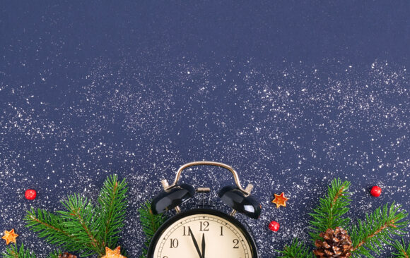 Christmas card. Brushing a branch of a tree on a dark blue background with red balls and figurines of shiny stars on white snow. Black retro alarm clock with stitches at 23.55 pm. Festive background Holiday Hours of Operation
