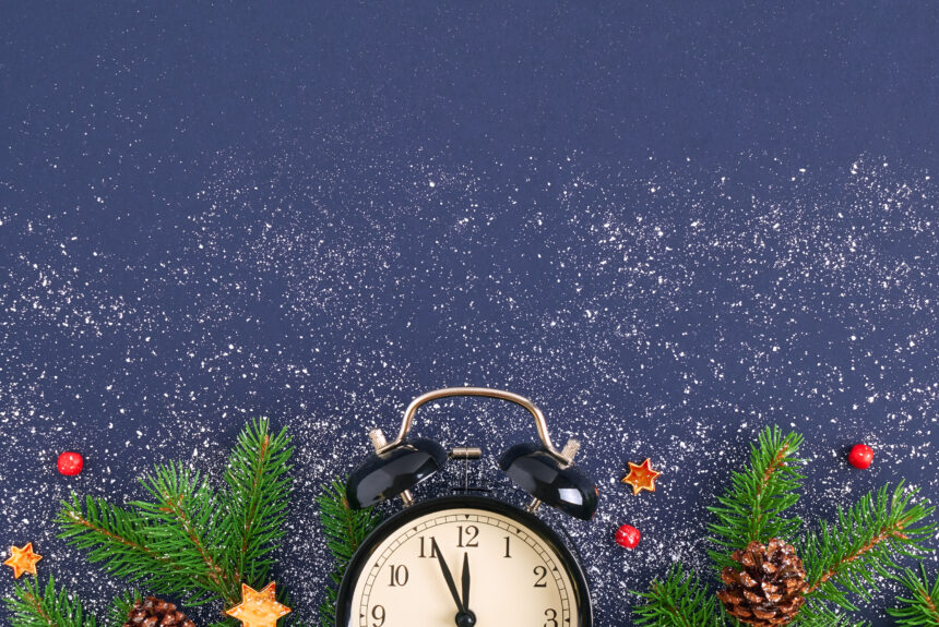 Christmas card. Brushing a branch of a tree on a dark blue background with red balls and figurines of shiny stars on white snow. Black retro alarm clock with stitches at 23.55 pm. Festive background Holiday Hours of Operation